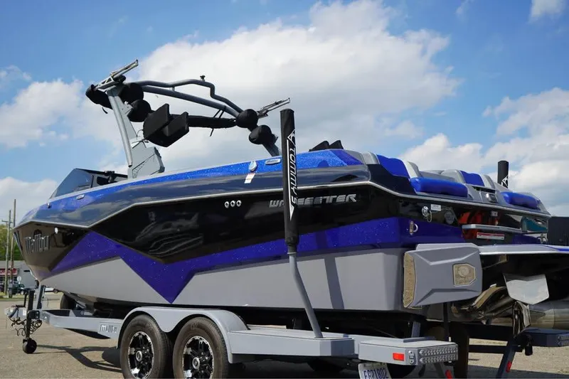 Slide: The Image of 2022 Malibu Wakesetter 25 LSV boat on trailer, blue and black design, under a cloudy sky. - 15
