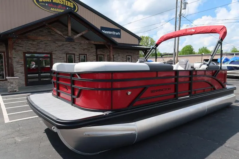 Slide: The Image of 2025 Bennington S Quad Bench 22 SSR pontoon boat in red, parked outside a dealership. - 18