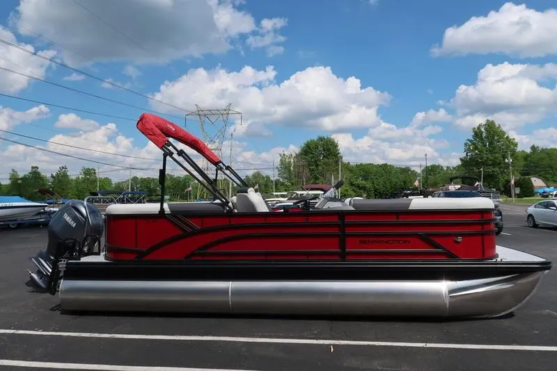 Slide: The Image of 2025 Bennington S Quad Bench 22 SSR pontoon boat, red and black, parked outdoors. - 2