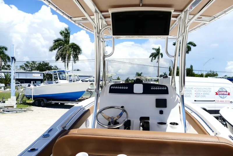 Slide: The Image of 2026 Pioneer 222 Islander boat interior with steering wheel, parked near palm trees and trailers. - 10