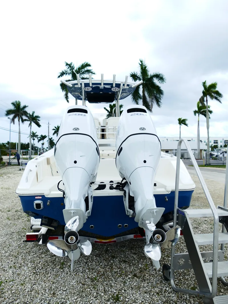 Slide: The Image of 2026 Bulls Bay 255CC boat with dual outboard motors, parked on gravel with palm trees. - 6