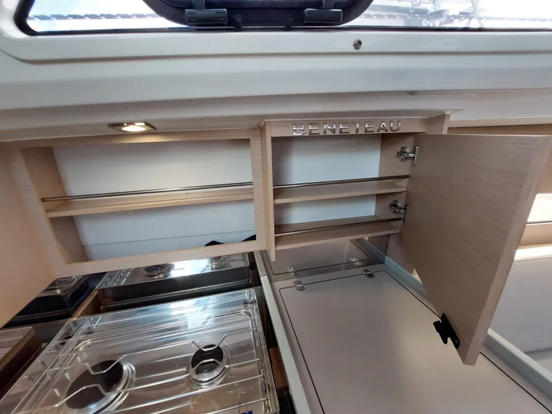 Slide: The Image of Interior of 2020 Beneteau Oceanis 30.1 yacht, featuring open wooden cabinets and a compact kitchen area. - 30