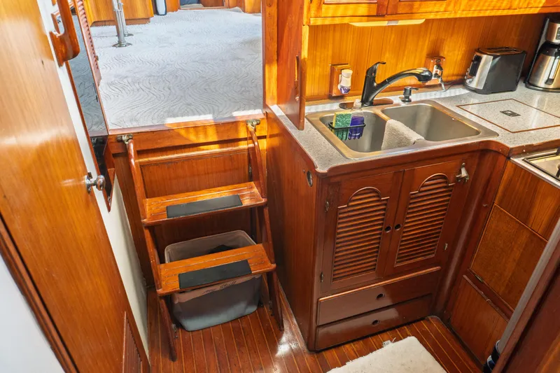 Slide: The Image of 1982 Albin 43 yacht interior with wooden cabinetry, compact kitchen, and steps leading to carpeted area. - 60