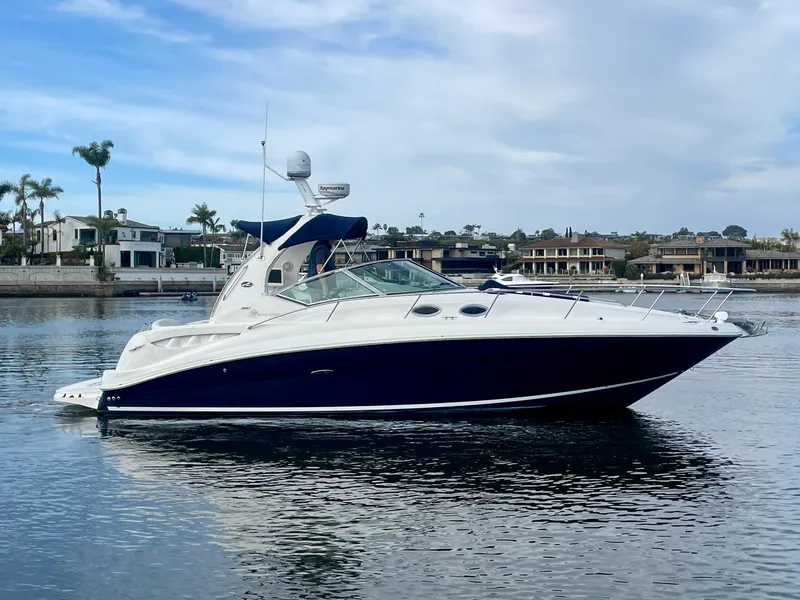 Slide: The Image of 2006 Sea Ray 320 Sundancer yacht on calm water, with coastal homes in the background. - 2