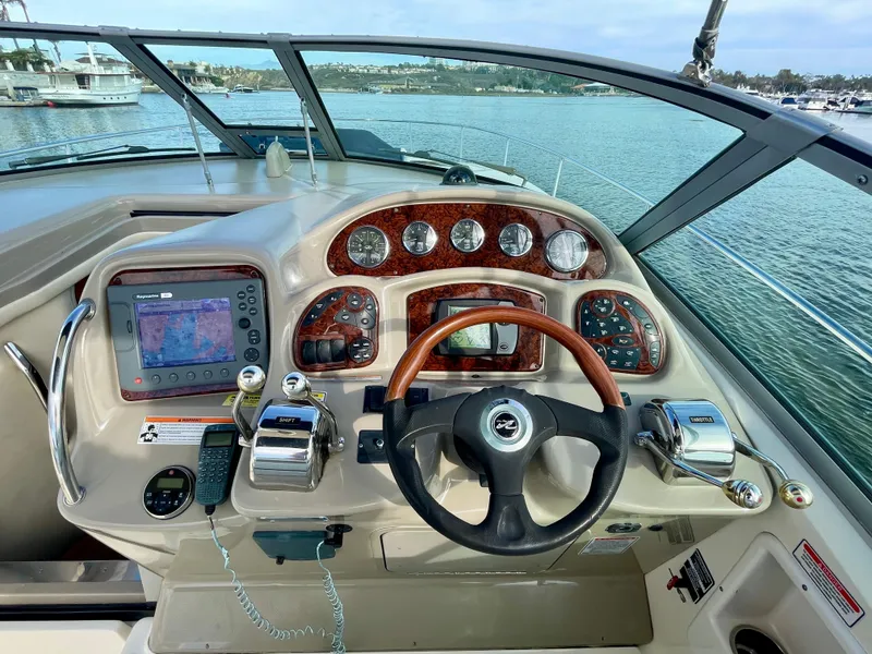Slide: The Image of 2006 Sea Ray 320 Sundancer helm with GPS, gauges, and steering wheel, docked on calm water. - 23