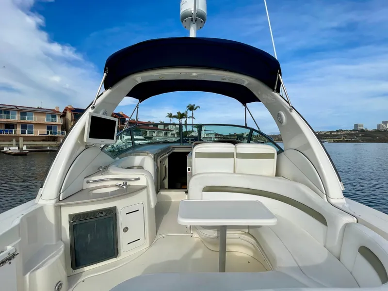 Slide: The Image of 2006 Sea Ray 320 Sundancer boat interior with seating and table, docked by waterfront homes. - 26