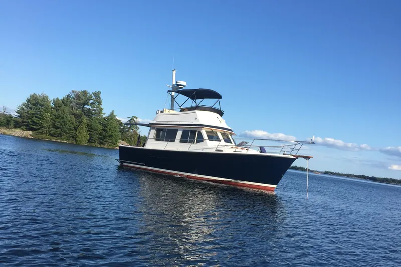 Slide: The Image of 1999 Sabreline 34 Flybridge boat on calm water, clear blue sky, and distant trees. - 0