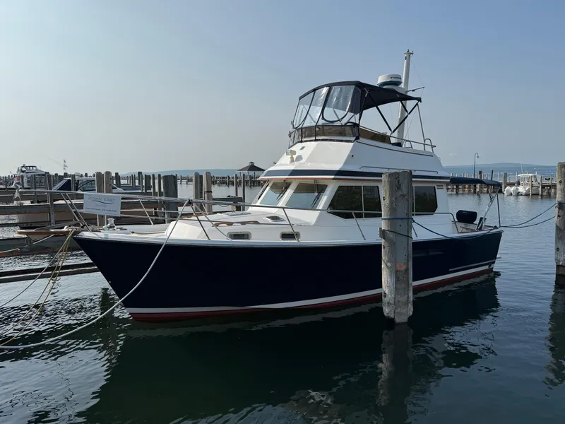 Slide: The Image of 1999 Sabreline 34 Flybridge boat docked at a marina, calm water, clear sky. - 1