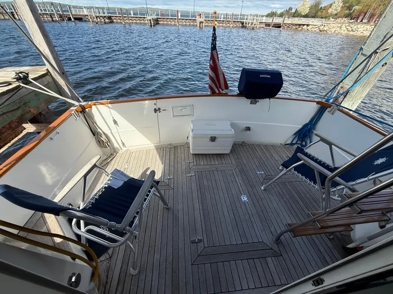 Slide: The Image of 1999 Sabreline 34 Flybridge boat deck with chairs, cooler, and American flag by the water. - 21