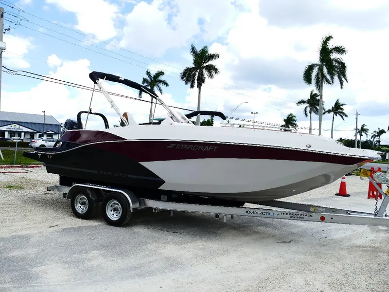 The Image of 2026 Starcraft SVX 231 OB boat on trailer, parked outdoors with palm trees in background. - 0