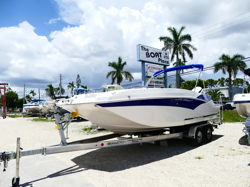 Slide: The Image of 2026 Starcraft SVX 231 OB DH boat on trailer at dealership, palm trees in background. - 4