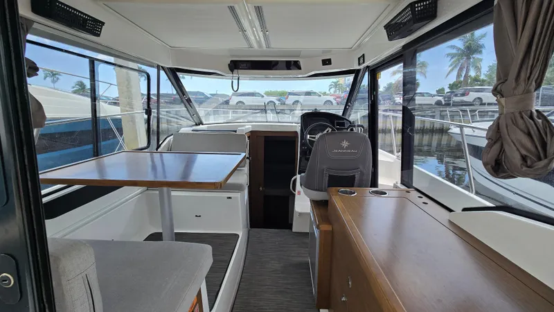Slide: The Image of 2019 Jeanneau NC895 interior with seating, table, and helm, docked by palm trees. - 5