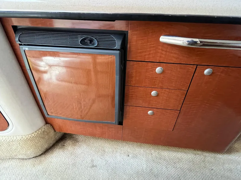 Slide: The Image of 2005 Sea Ray 300 Sundancer interior with wood cabinetry and compact refrigerator. - 21