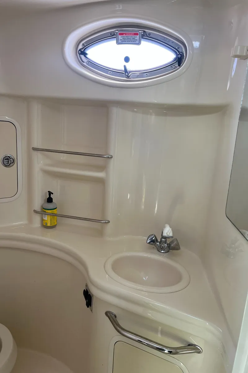 Slide: The Image of 2005 Sea Ray 300 Sundancer bathroom with sink, oval window, and storage shelves. - 26
