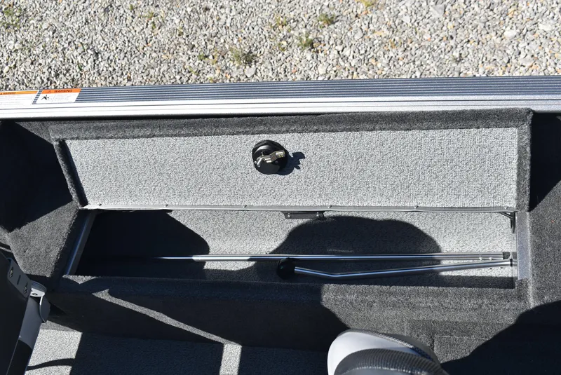 Slide: The Image of 2014 Lund 1675 Impact SS boat storage compartment with latch, open on gravel background. - 12