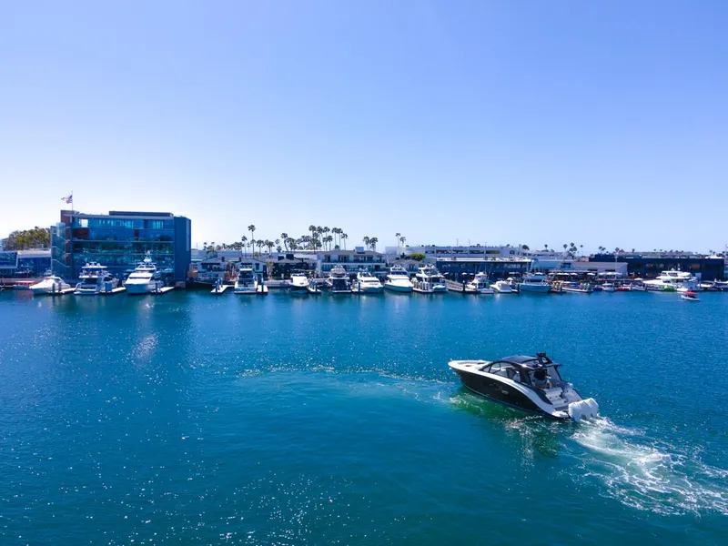 Slide: The Image of 2022 Sea Ray Sundancer 370 OB cruising in a marina with docked boats and clear blue sky. - 18