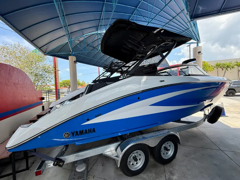 Slide: The Image of 2025 Yamaha Boats 255XD in blue and white on a trailer under a canopy. - 2