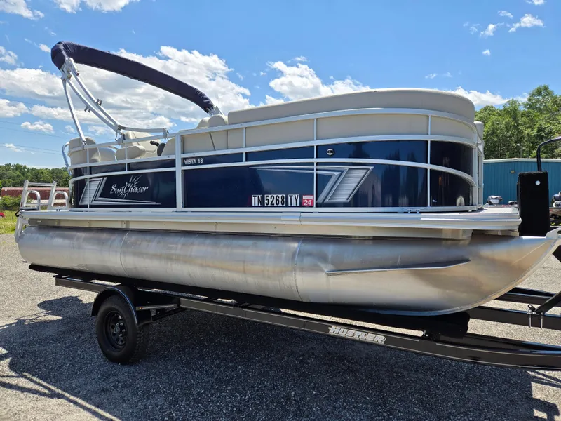 Slide: The Image of 2023 SunChaser Vista 18 LR pontoon boat on trailer, blue and white design, sunny day. - 3