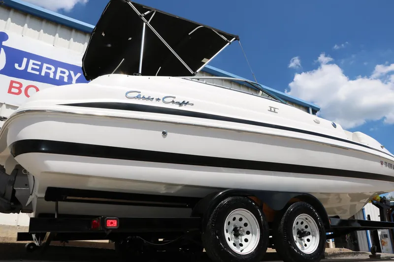 Slide: The Image of 2000 Chris-Craft 232 boat on trailer, white with black accents, under a clear blue sky. - 2