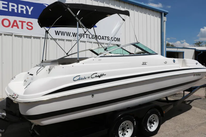 Slide: The Image of 2000 Chris-Craft 232 boat on trailer, white with black accents, parked outside a dealership. - 3
