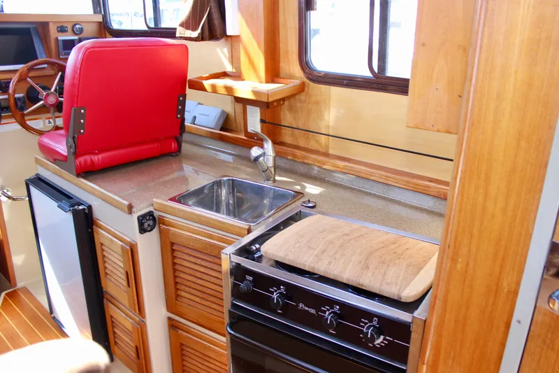 Slide: The Image of 2011 Ranger Tugs R-27 interior with kitchen, sink, stove, and red seat. - 23