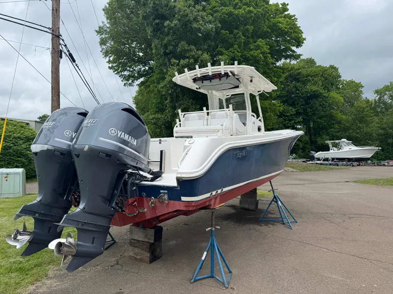 Slide: The Image of 2013 Edgewater 318CC boat with twin Yamaha engines on stands, surrounded by trees. - 2