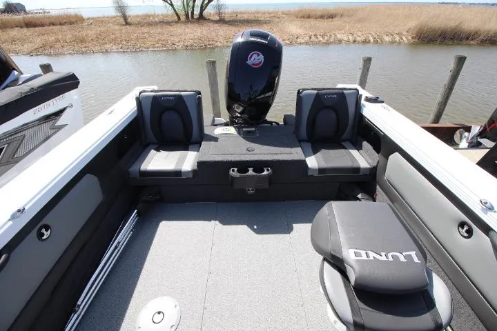 Slide: The Image of 2025 Lund 1975 Tyee boat interior with seating and motor, near a calm waterway. - 3