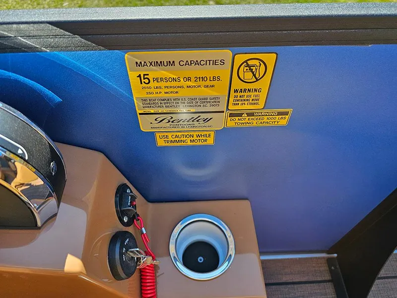 Slide: The Image of 2025 Bentley Pontoons 223 Elite Swingback console with capacity warning labels and cup holder. - 27