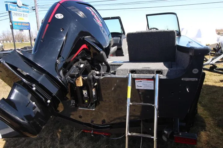 Slide: The Image of 2025 Lund 1775 Crossover XS boat with outboard motor and ladder, parked on grass. - 2