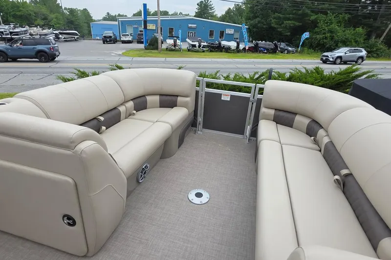 Slide: The Image of 2025 Sun Tracker PB 22 DLX pontoon boat with beige seating, parked near a dealership. - 9