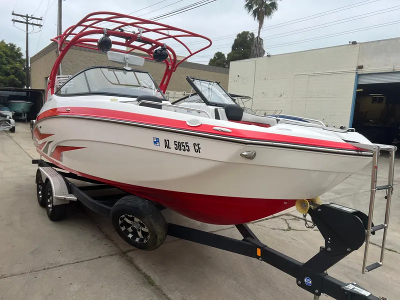 Slide: The Image of 2020 Yamaha Boats 242X in red and white on a trailer, parked outdoors. - 7
