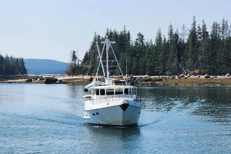 Slide: The Image of 2003 Nordhavn N46 yacht cruising in a serene, forested coastal area. - 2