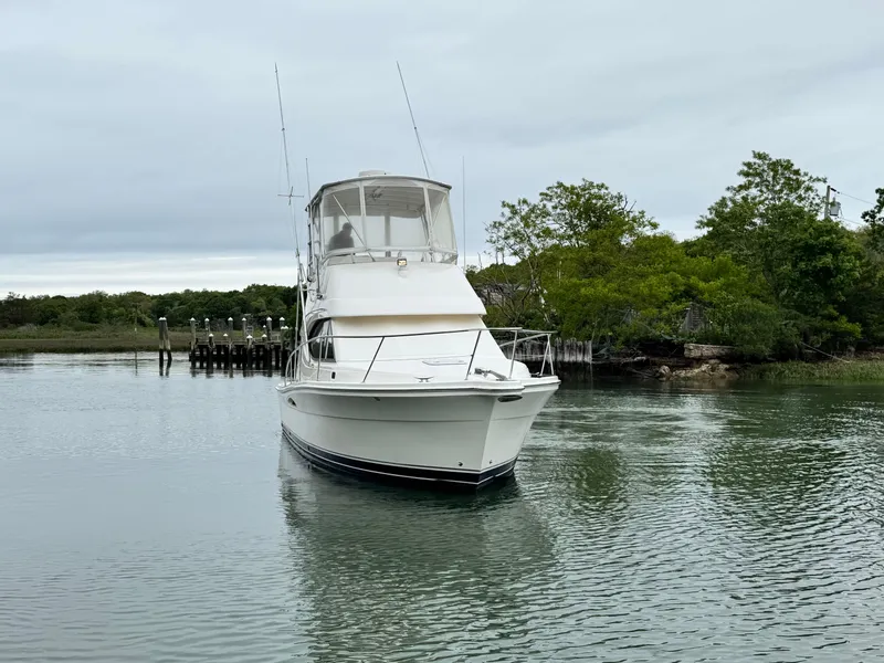Slide: The Image of 2005 Riviera 33 Flybridge boat on calm water near lush greenery. - 3