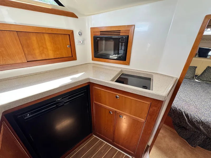 Slide: The Image of 2005 Riviera 33 Flybridge kitchen with microwave, fridge, and wooden cabinetry. - 30