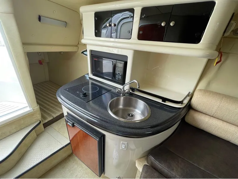 Slide: The Image of Compact kitchen area in a 2006 Monterey 250 CR boat, featuring a sink, stove, and microwave. - 19