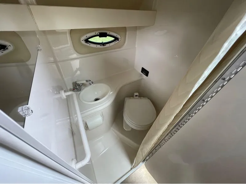 Slide: The Image of Compact bathroom in a 2006 Monterey 250 CR boat, featuring a toilet, sink, and porthole window. - 7