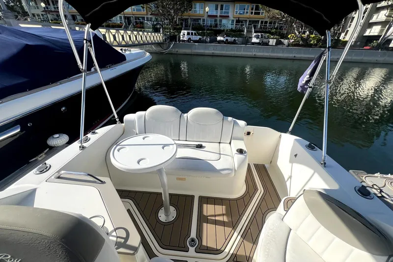 Slide: The Image of 2006 Sea Ray 240 Sundancer boat interior with seating and table, docked by waterfront. - 10