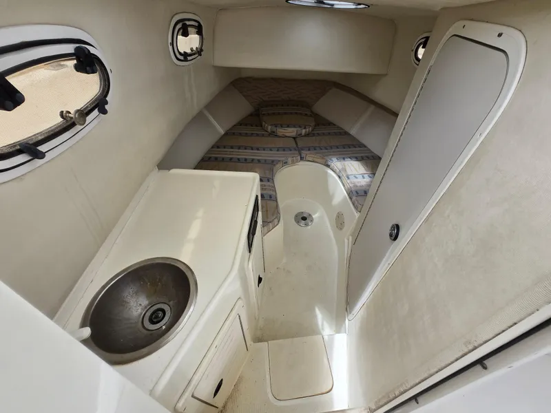 Slide: The Image of 1999 Mako 253 Walk Around cabin interior with sink, bed, and portholes. - 1