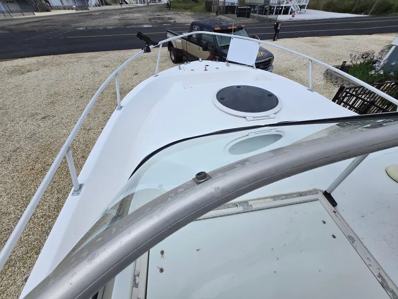 Slide: The Image of 1999 Mako 253 Walk Around boat deck with windshield and hatch, parked on gravel. - 11