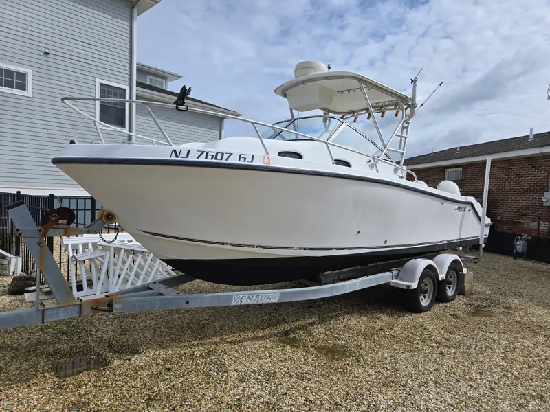 Slide: The Image of 1999 Mako 253 Walk Around boat on trailer, parked outdoors, with overcast sky. - 5