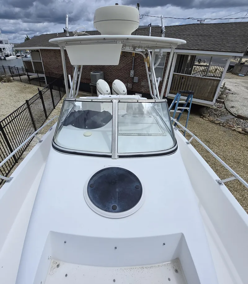 Slide: The Image of 1999 Mako 253 Walk Around boat with white deck and cabin, docked near a house. - 8