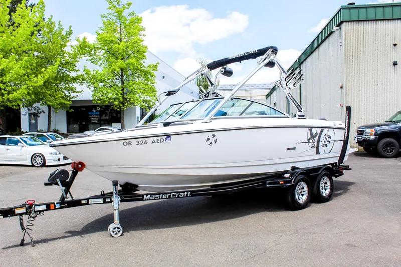 Slide: The Image of 2010 MasterCraft X-15 boat on trailer, parked outdoors near trees and buildings. - 1