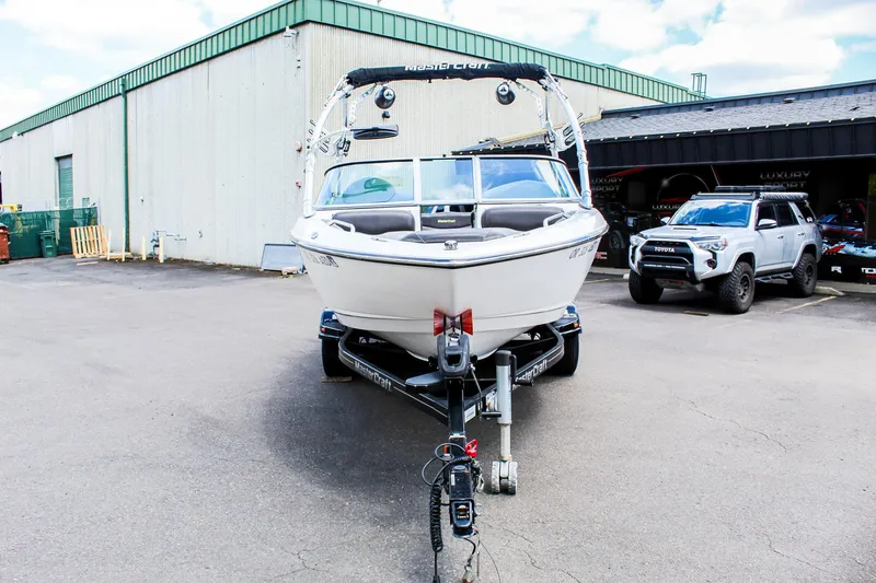 Slide: The Image of 2010 MasterCraft X-15 boat on trailer in parking lot, near vehicles and warehouse. - 4