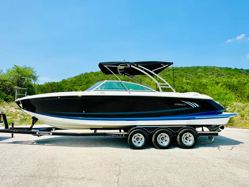 Slide: The Image of 2012 Cobalt A28 boat on trailer, black hull, sleek design, sunny day, green hills background. - 10