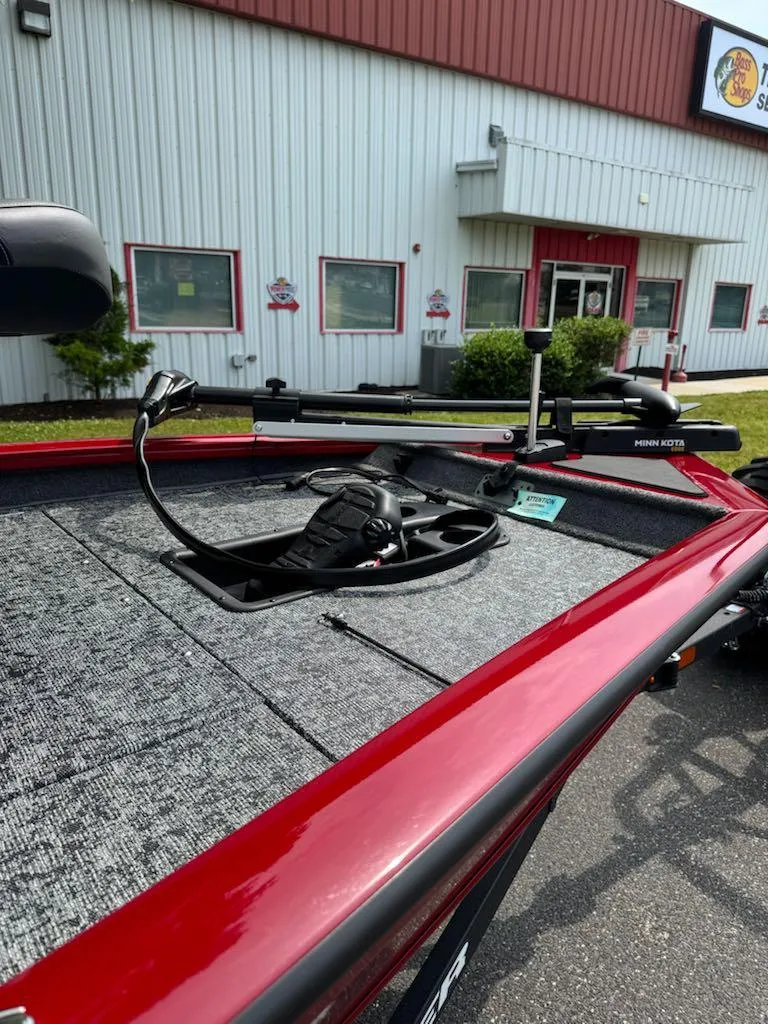 Slide: The Image of 2025 Tracker Pro Team 175 boat with Minn Kota trolling motor, parked outside a building. - 7
