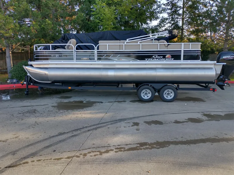 The Image of 2025 Sun Tracker SportFish 22 DLX pontoon boat on trailer, parked outdoors. - 0