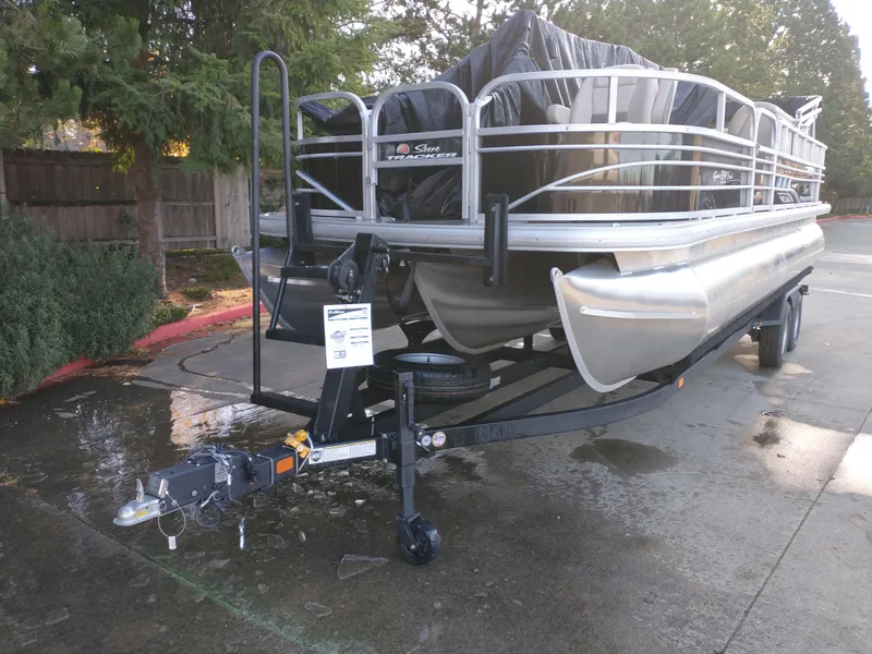 Slide: The Image of 2025 Sun Tracker SportFish 22 DLX pontoon boat on trailer, parked outdoors. - 2