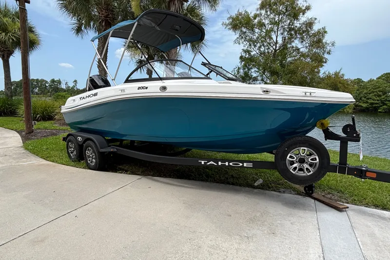 The Image of 2025 Tahoe 200 S boat on trailer by lakeside, surrounded by palm trees. - 0