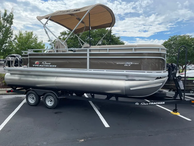 The Image of 2025 Sun Tracker SportFish 20 DLX pontoon boat on trailer in parking lot. - 0