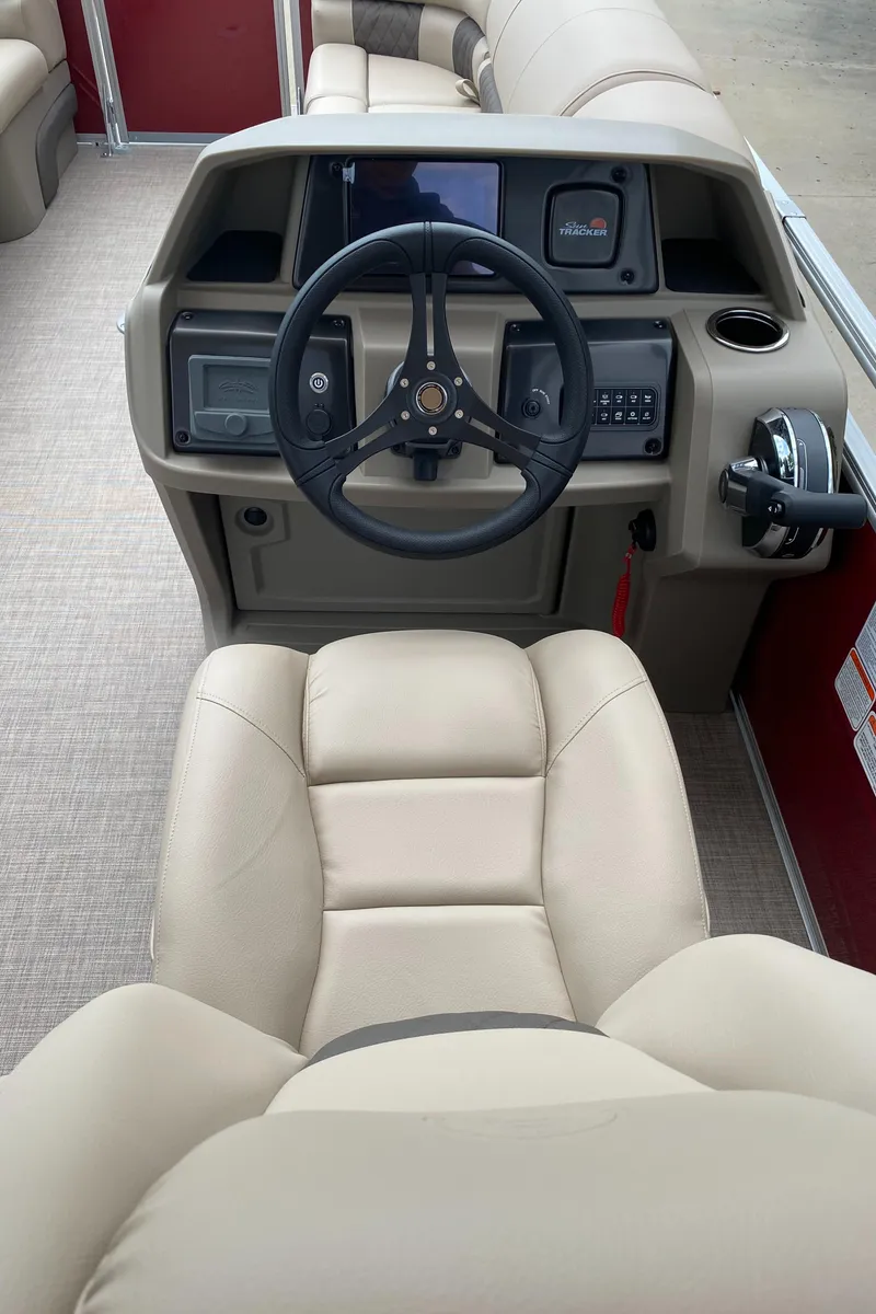 Slide: The Image of 2025 Sun Tracker Party Barge 22 DLX helm with beige seating and modern controls. - 6